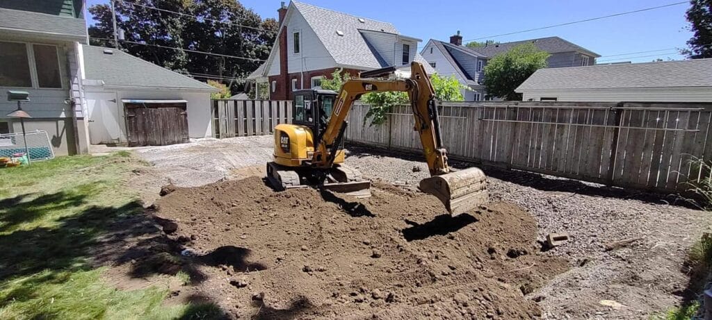 Compact excavator grading soil in a residential backyard as part of a site preparation project by M. Riddle Excavating in Ontario.