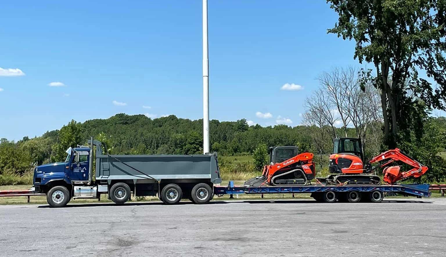 Canadian flag flying above excavation equipment and a dump truck from M. Riddle Excavating on a clear day in Kingston, Ontario.