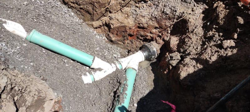 Partially buried PVC sewer line connection exposed in a gravel trench during underground utility installation.