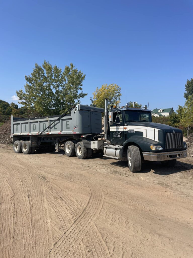 Riddle Aggregates dump truck parked on a construction yard with clear blue sky and trees in the background