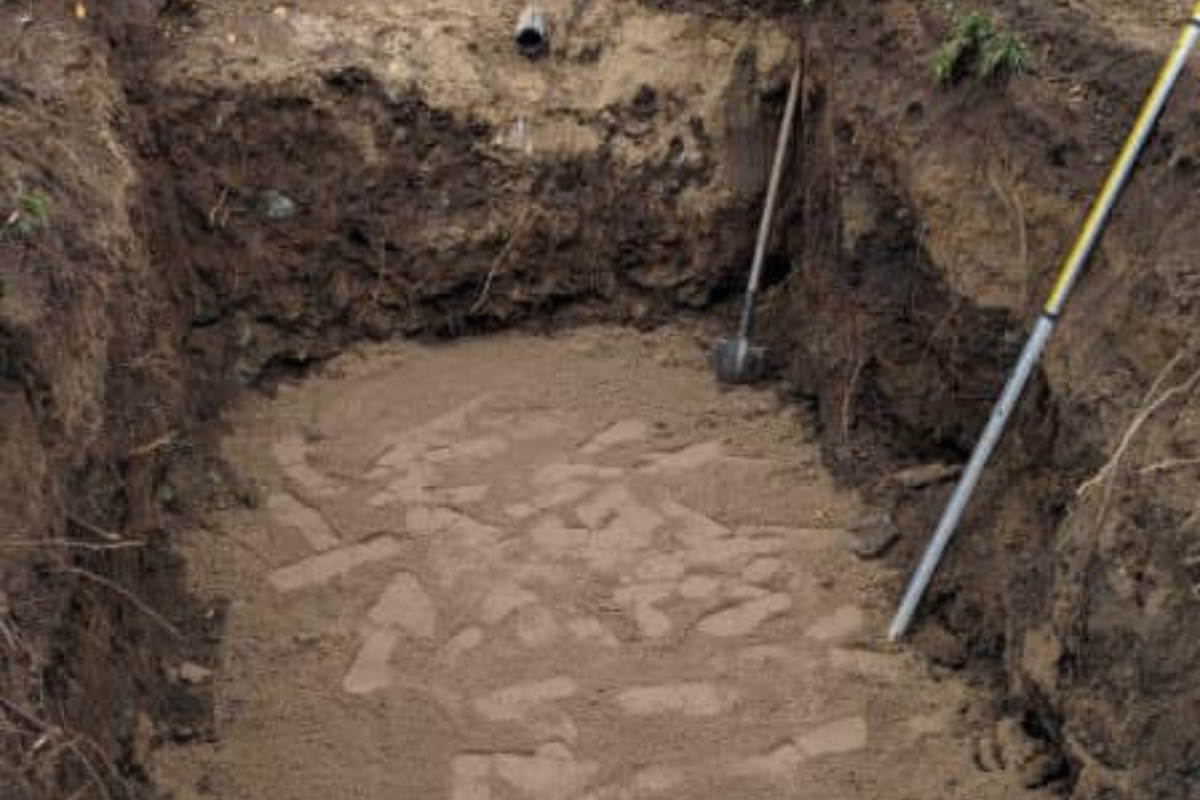 Excavation complete and base layer of sand placed for tank installation next to foundation wall.