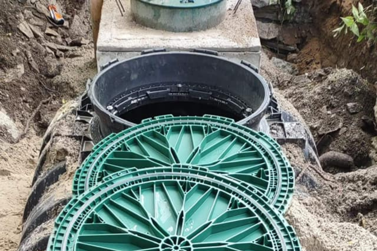 Close-up of a septic tank with the lid off, showing the open access riser and green lids placed beside it during installation.