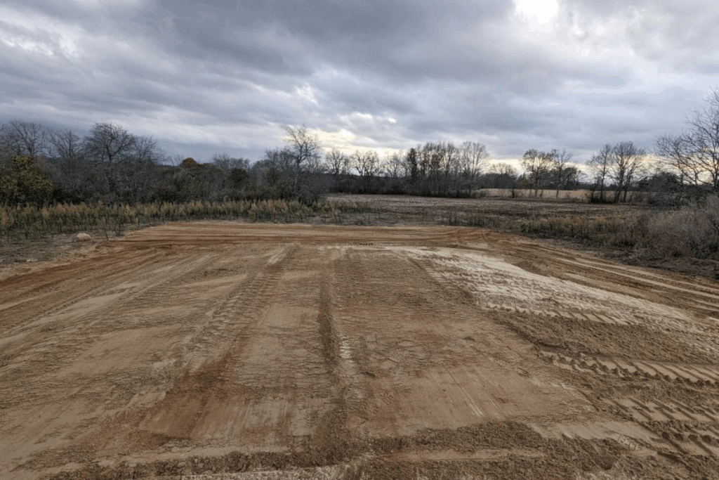 Completed septic installation site, fully backfilled and restored with open field and trees in background. Protect a septic drain field in winter.