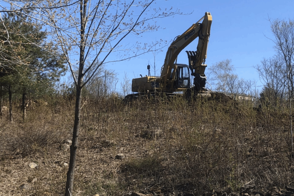 Excavator clearing brush and grading slope on wooded residential lot in Parham.