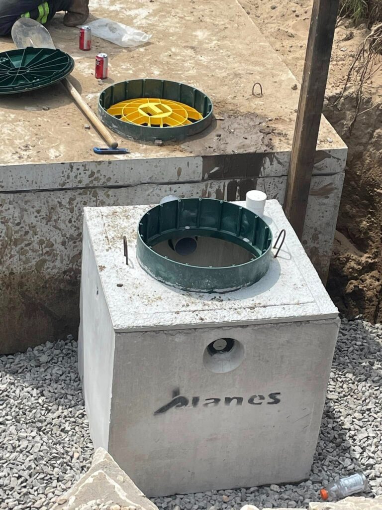 Concrete septic tank distribution system installation with green and yellow access covers, surrounded by gravel base for stability.