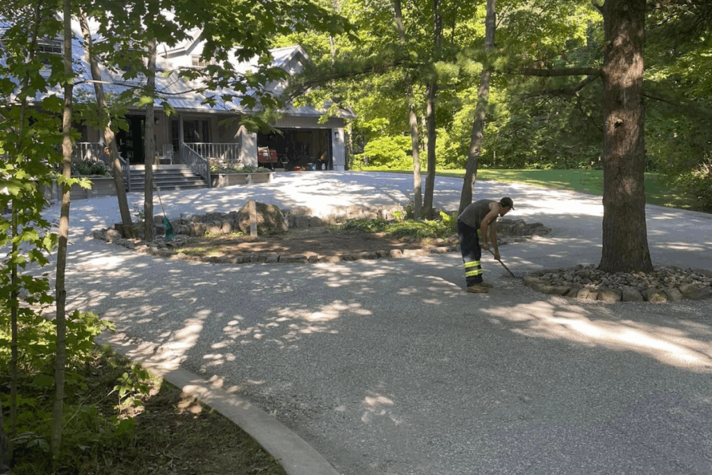 Shaded driveway curve through dense forest with a crew member walking along the gravel edge.