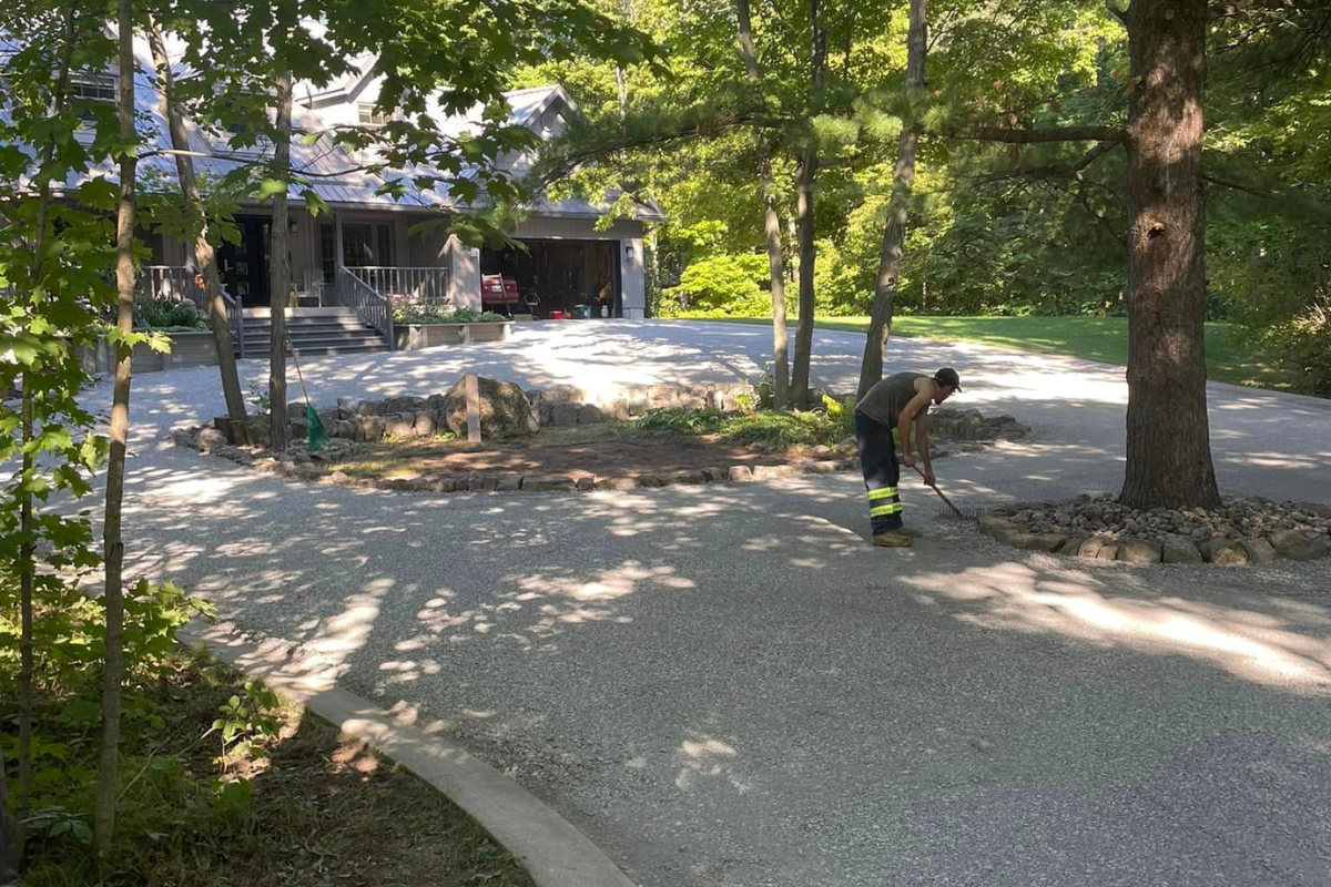 Shaded driveway curve through dense forest with a crew member walking along the gravel edge.
