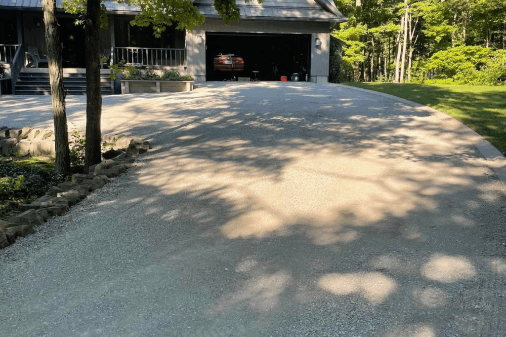 Freshly compacted gravel driveway leading to a two-car garage in front of a modern home surrounded by trees.
