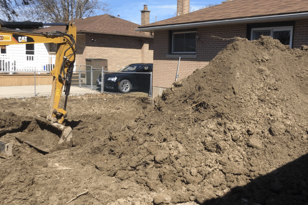 Excavator beside a large pile of soil on a residential excavation site.