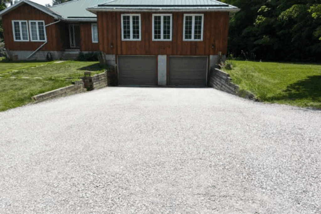 Wide view of a newly graded and compacted gravel driveway leading to a two-car garage on a residential property.