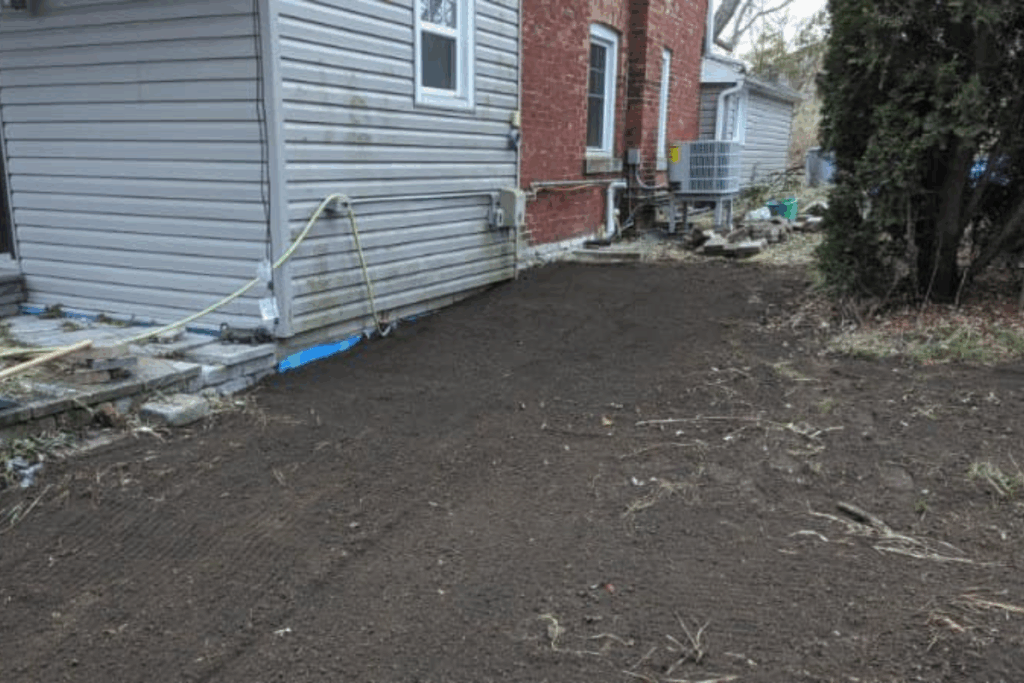 Backfilled and graded area along the side of a house following foundation waterproofing work.