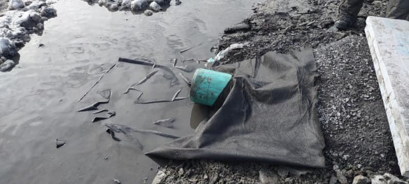 Excavation site showing geotextile fabric exposed beneath pooled water, with gravel and construction materials visible during ground preparation.