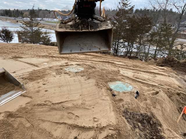 An excavator hovering over a septic system with snow in the background.